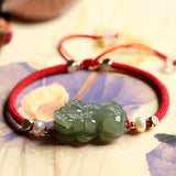 Green jade beaded bracelet with Pixiu charm and red string, a symbolic accessory for wealth manifestation and abundance.