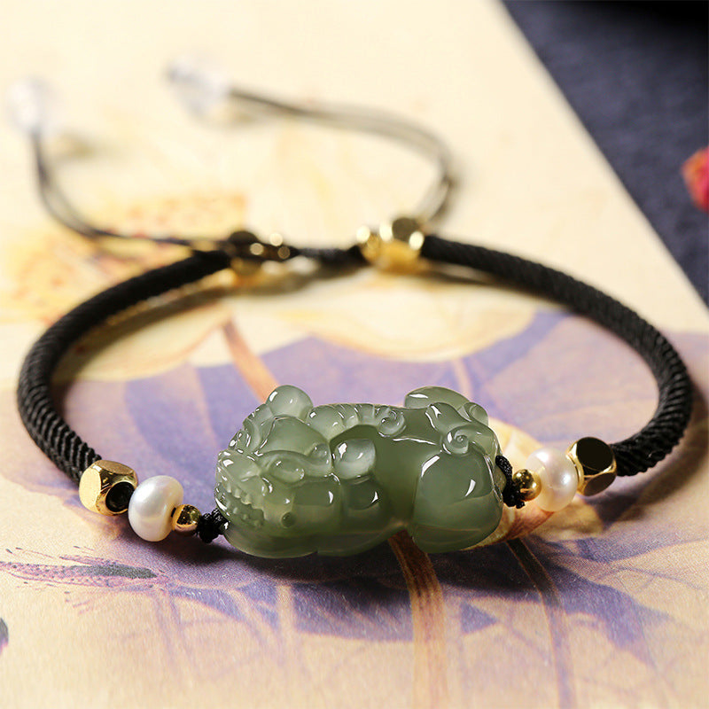 Black string bracelet with green jade Pixiu charm for wealth manifestation, includes beaded green jade and pearl details.
